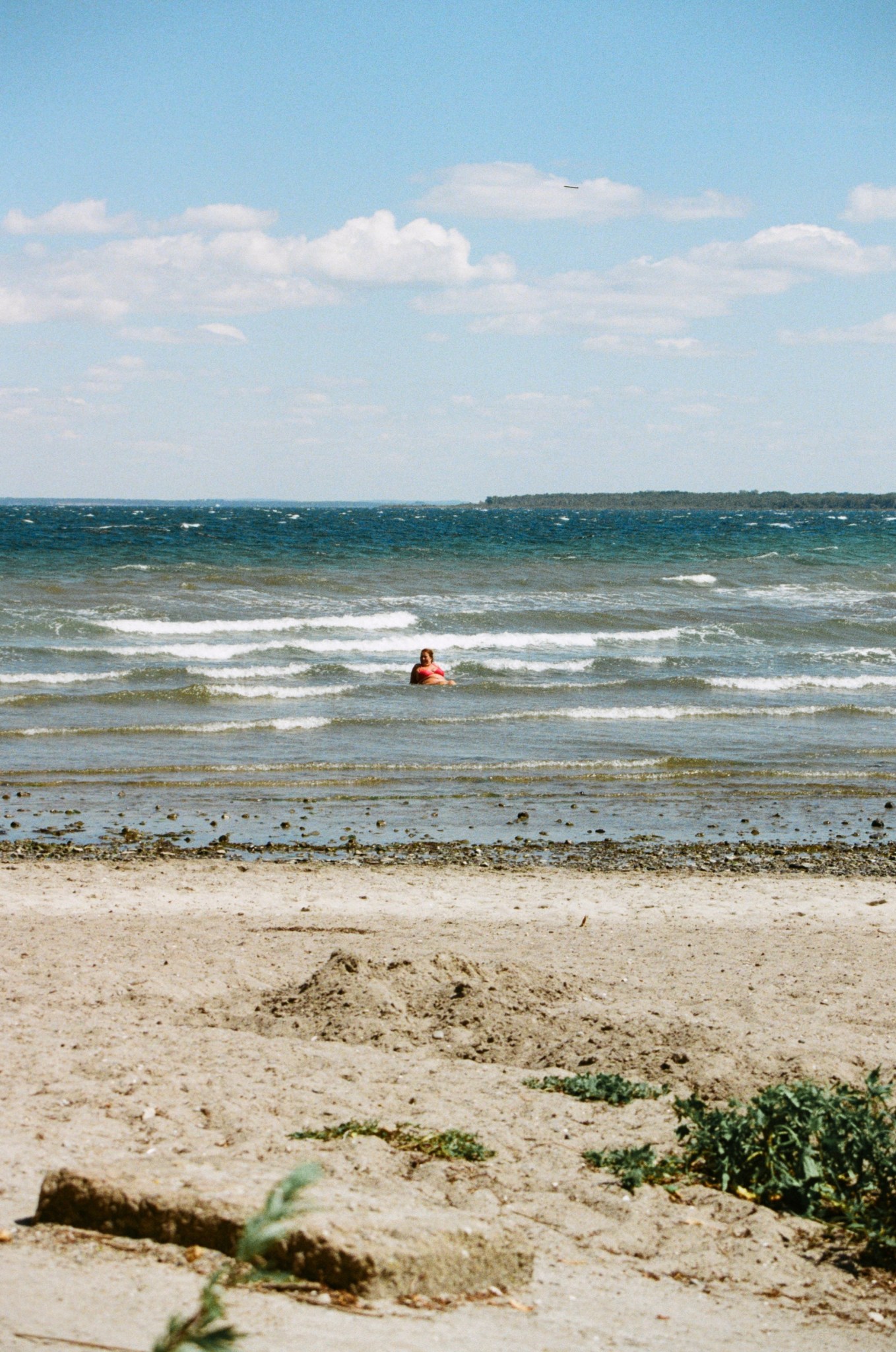 Ein Bild vom Strand. Eine Person sitzt im Wasser.
